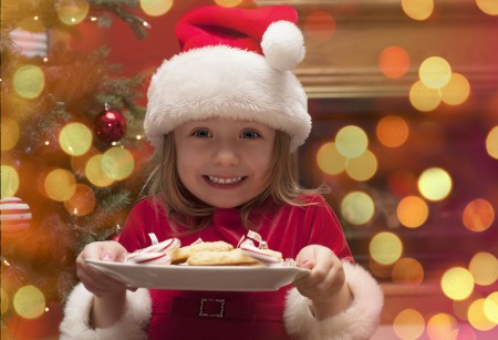 young girl holding a plate of cookies and candy while wearing a santa hat for the pediatric dentist in katy
